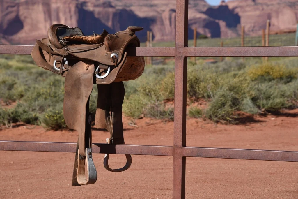 A large Western saddle placed on a fence.