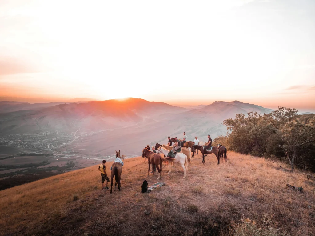 Horses-and-riders-with-sunset Group of horseback riders on a mountain ridge watching a scenic sunset over distant peaks