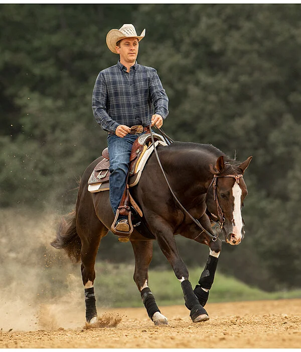 A western rider performing a maneuver on a dark brown horse wearing complete western tack and black sport boots for leg protection.